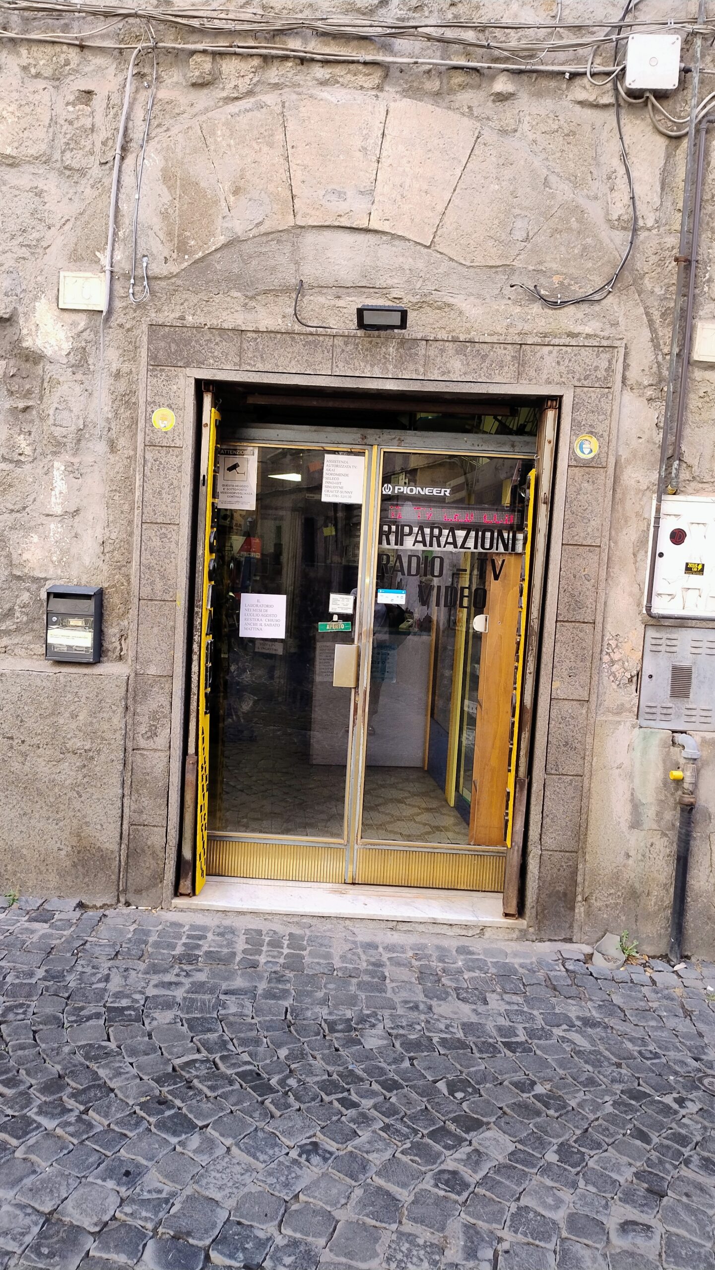 Un negozio di riparazioni radio, TV e video nel centro storico di Viterbo, con il cartello Aperto sulla porta a vetri