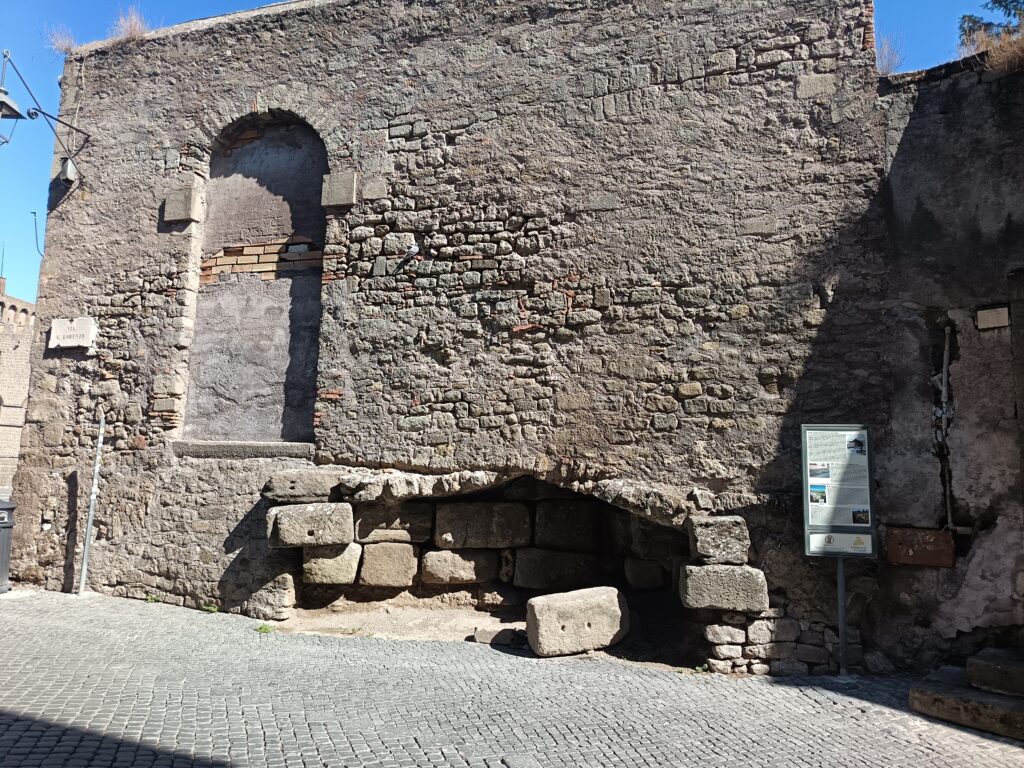 Blocchi di pietra antichi alla base di un muro medievale in via San Lorenzo a Viterbo, con un pannello informativo