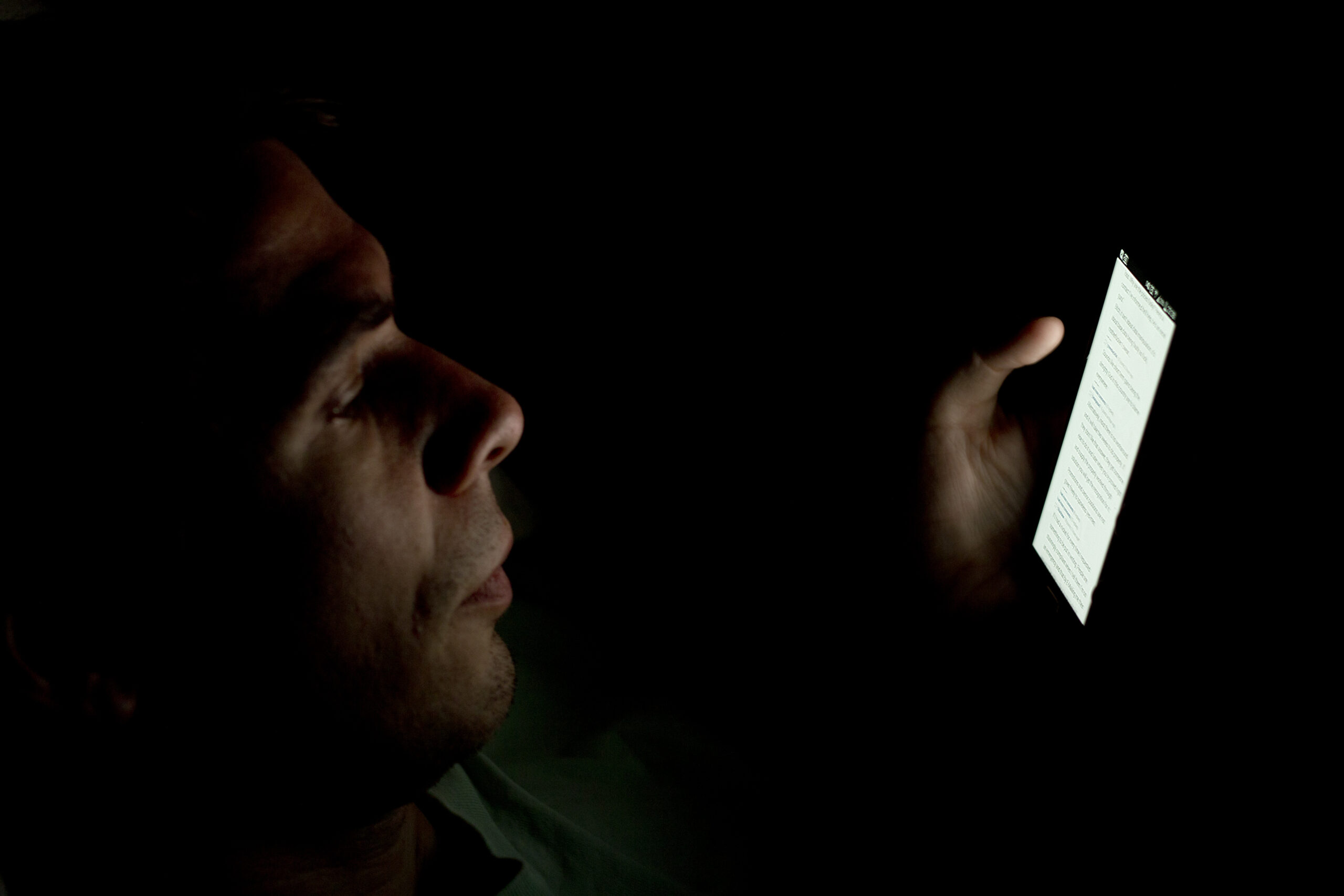 Una persona illuminata solo dallo schermo dello smartphone, al buio