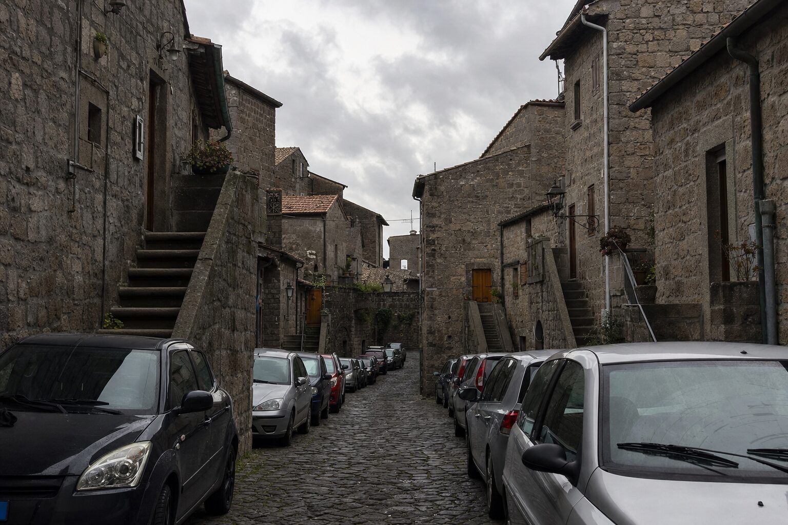 Vicolo medievale con case in pietra e profferli, congestionato da auto parcheggiate su entrambi i lati