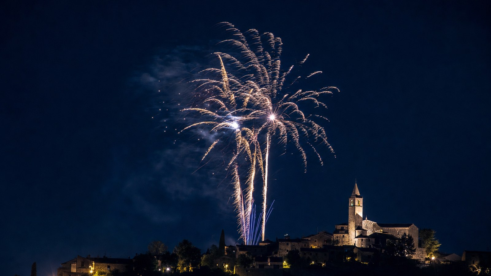 Fuochi d'artificio esplodono nel cielo notturno sopra un borgo collinare