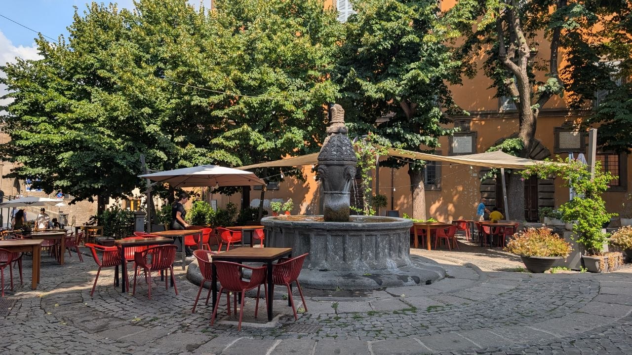 La fontana duecentesca al centro di Piazza della Morte, circondata dai tavolini dei locali