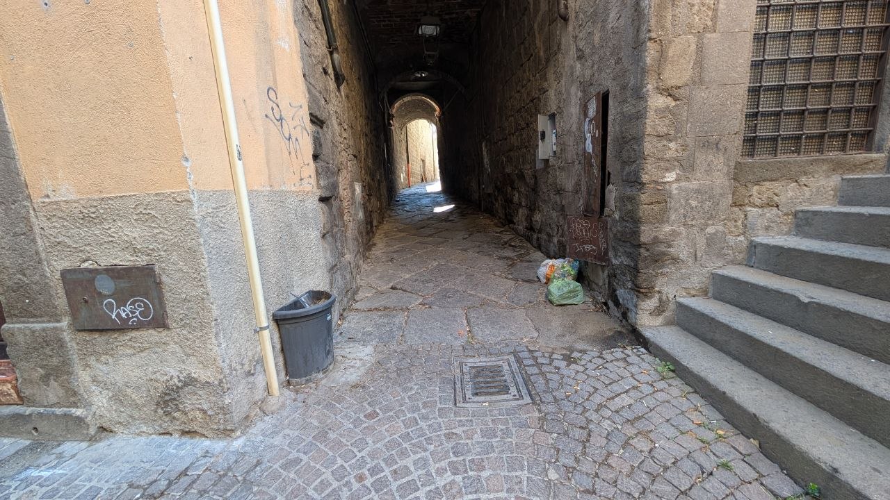 Via degli Scalzi vista dal fondo: il vicolo stretto, i sacchetti di rifiuti e i graffiti sulle pareti