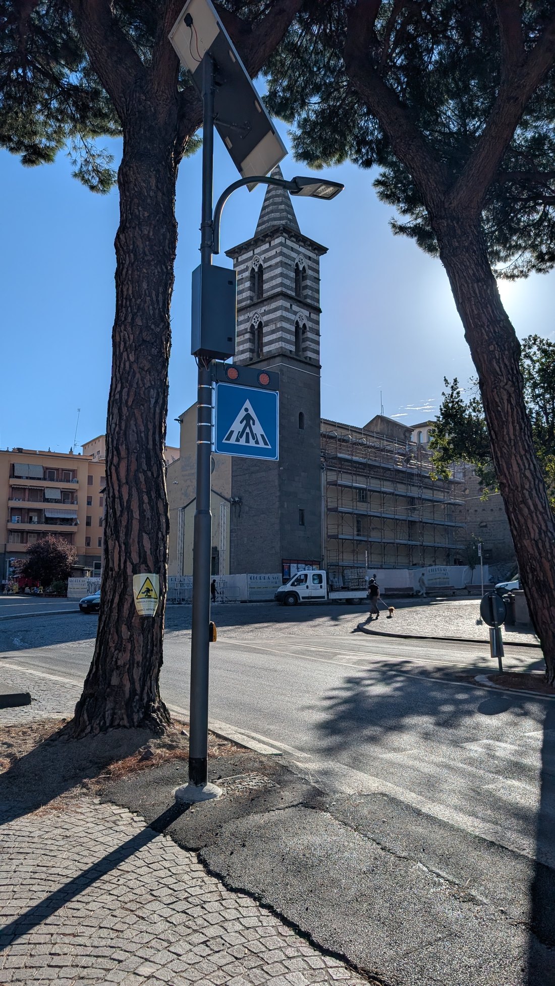 L'attraversamento pedonale illuminato in piazza dei Caduti, al Sacrario, con il palo dotato di pannello solare e la colonnina gialla del pulsante
