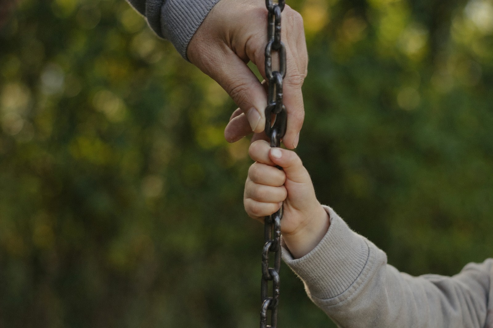 La mano di un adulto e quella di un bambino sulla catena di un'altalena