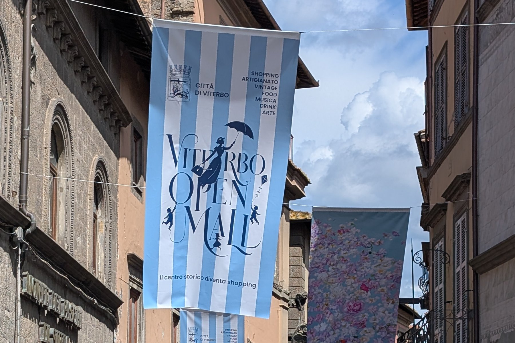 Stendardi di Viterbo Open Mall appesi tra i palazzi di una via del centro storico di Viterbo