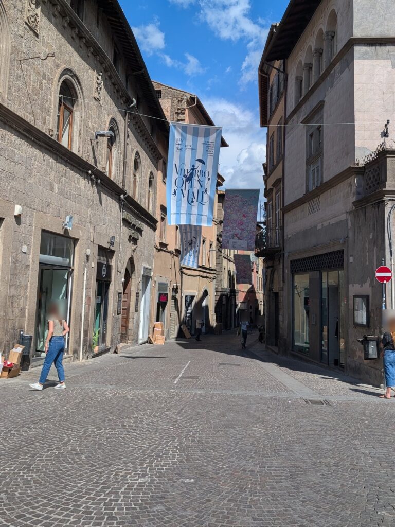 Stendardo a strisce azzurre di Viterbo Open Mall in una via del centro storico, con passanti