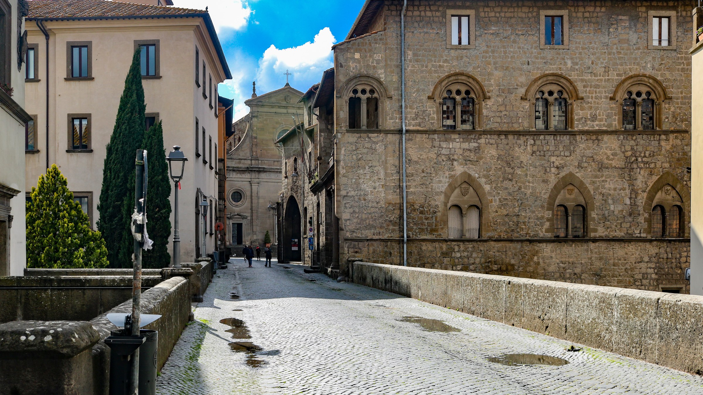 Una via lastricata del centro storico di Viterbo, fra un palazzo medievale in pietra e una chiesa sullo sfondo