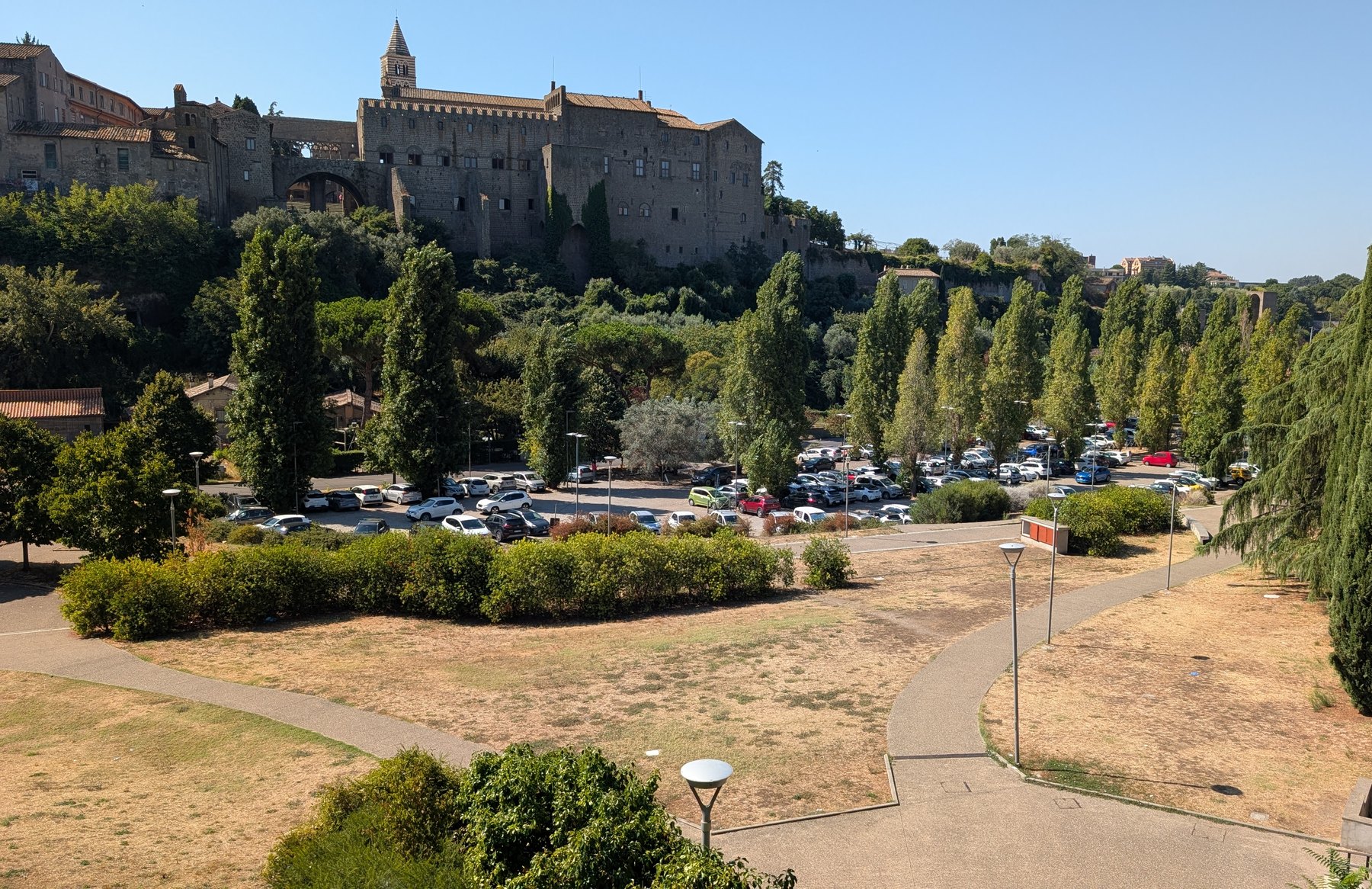 Valle Faul a Viterbo: prati secchi e vuoti, il parcheggio pieno di auto e sullo sfondo il Palazzo dei Papi