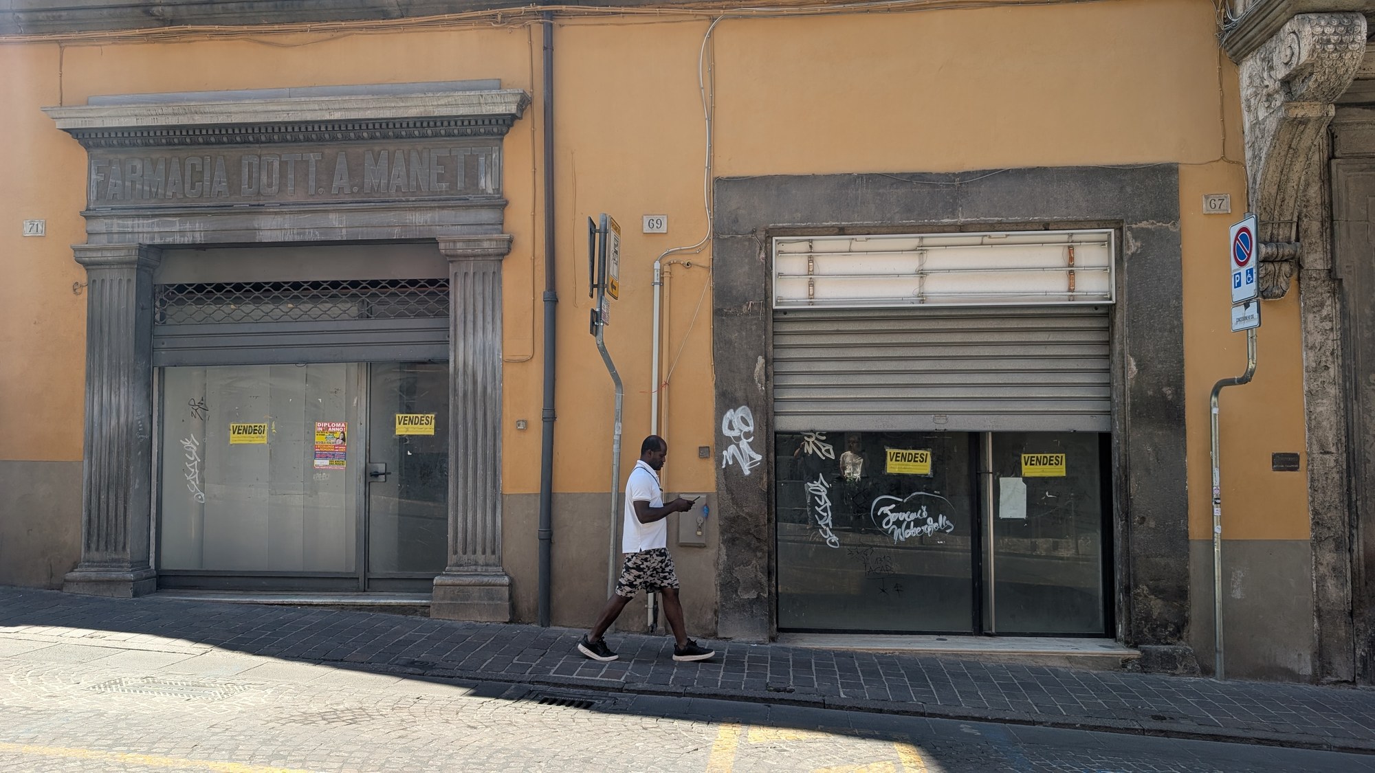 Due saracinesche chiuse con cartelli di affitto in una strada del centro storico di Viterbo, una persona cammina davanti