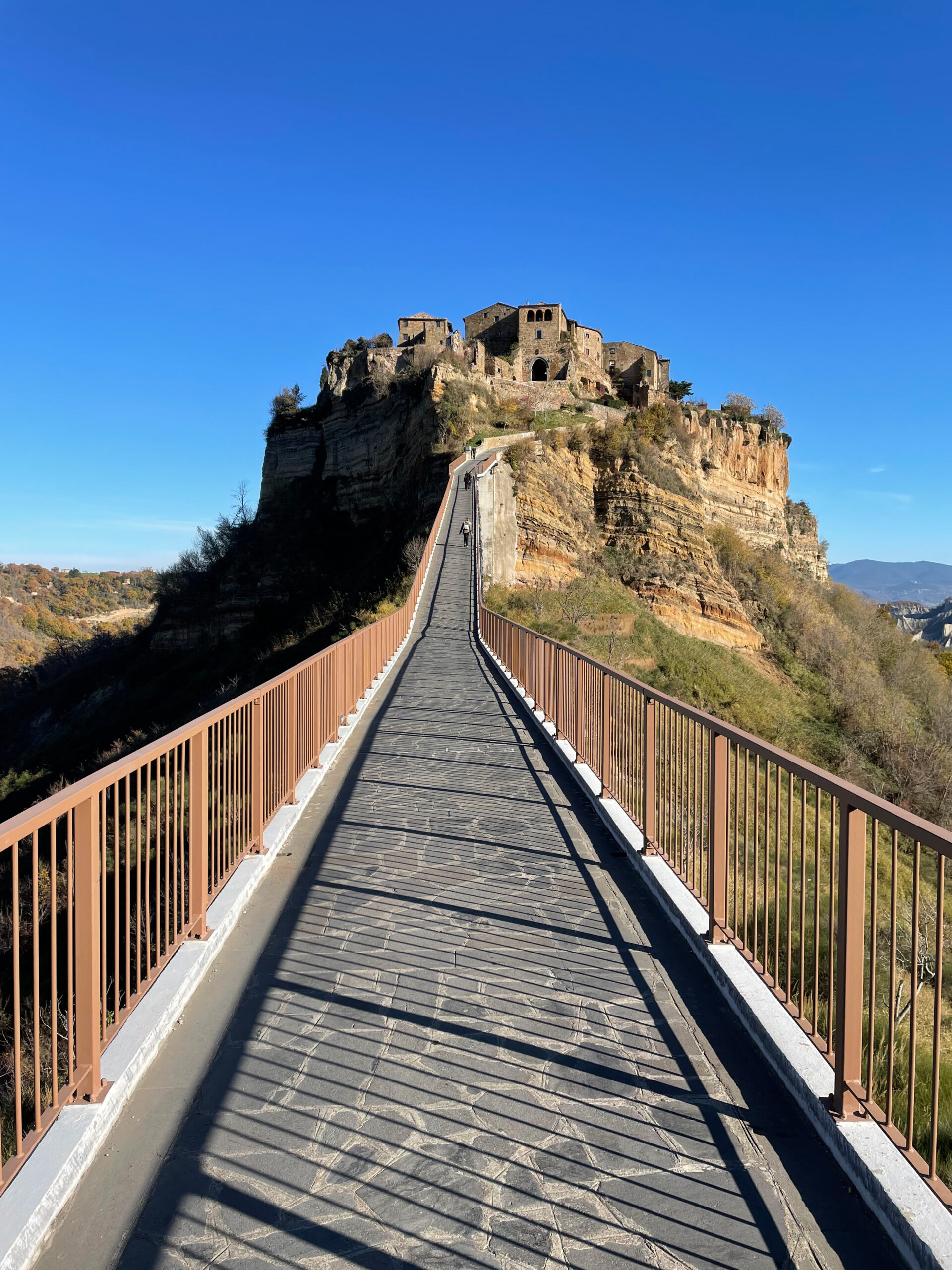 Il ponte pedonale che sale verso il borgo di Civita di Bagnoregio, arroccato sulla rupe di tufo, sotto un cielo azzurro