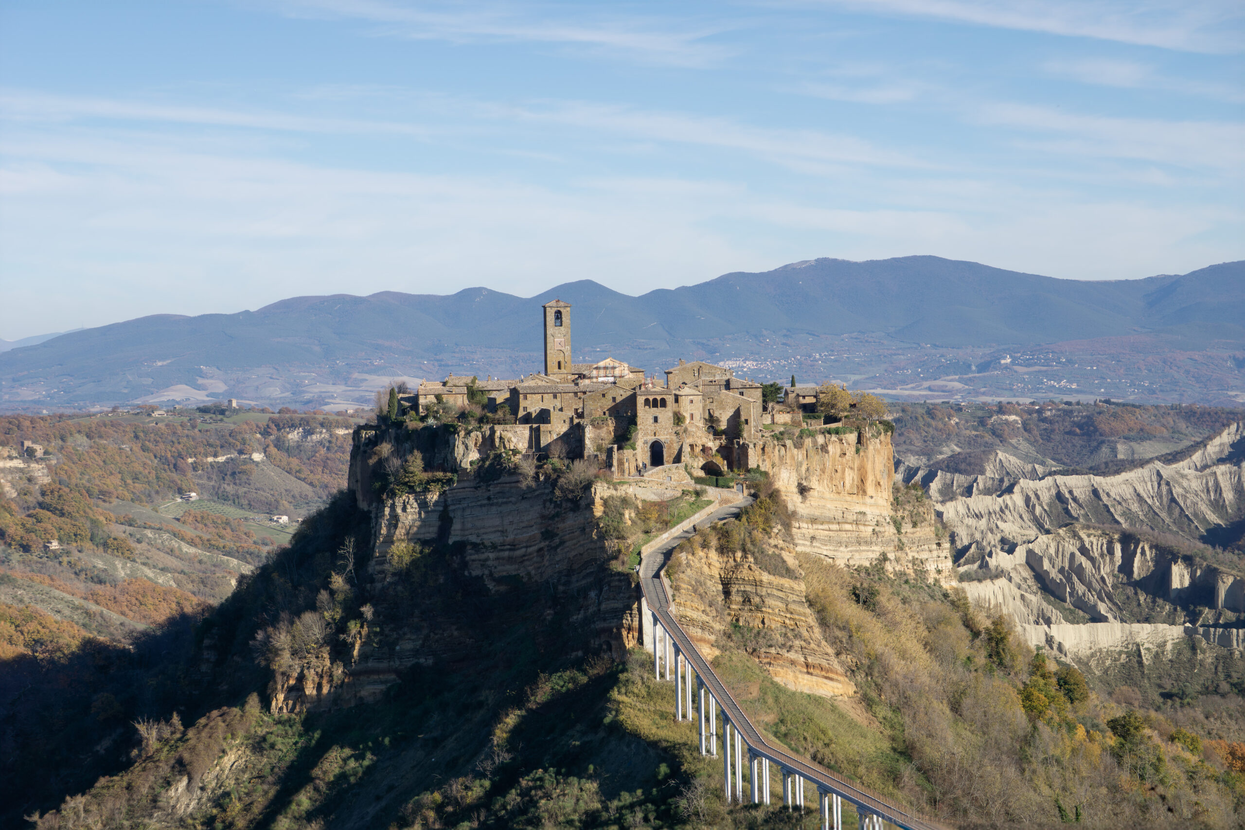 Il borgo di Civita di Bagnoregio sulla rupe di tufo, con il campanile, il lungo ponte pedonale e i calanchi in luce autunnale