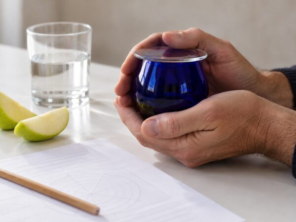 Due mani scaldano un bicchierino blu da assaggio dell’olio su un banco di analisi sensoriale