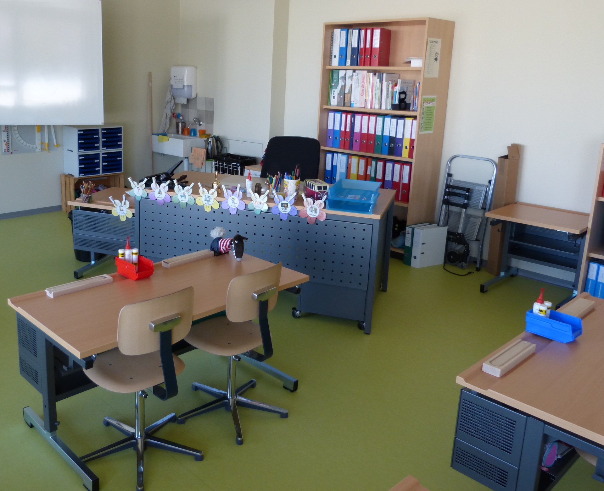 Aula scolastica con banchi, sedie e scaffali con raccoglitori colorati