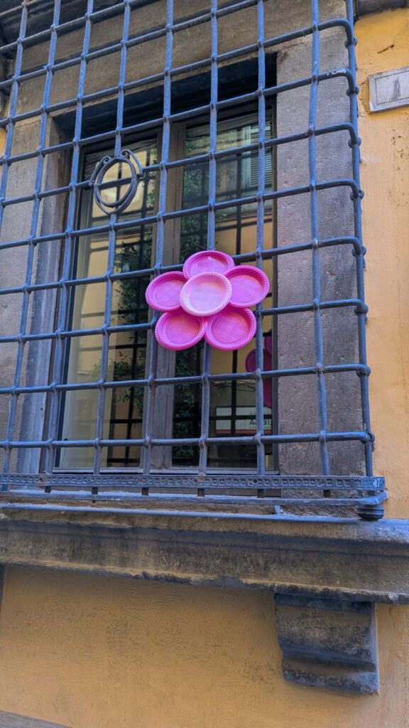 Un fiore fatto con piatti di plastica rosa legato a una grata