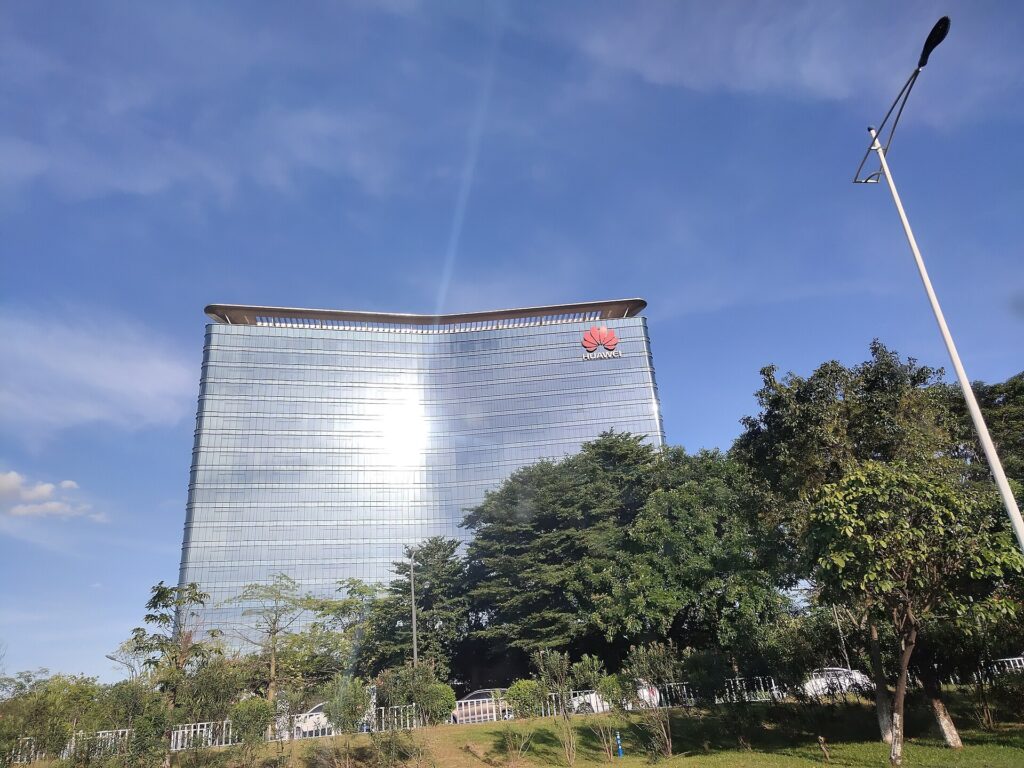 La torre a vetri di Huawei a Songshan Lake, a Dongguan, con il logo dell’azienda in cima, dietro gli alberi di un parco