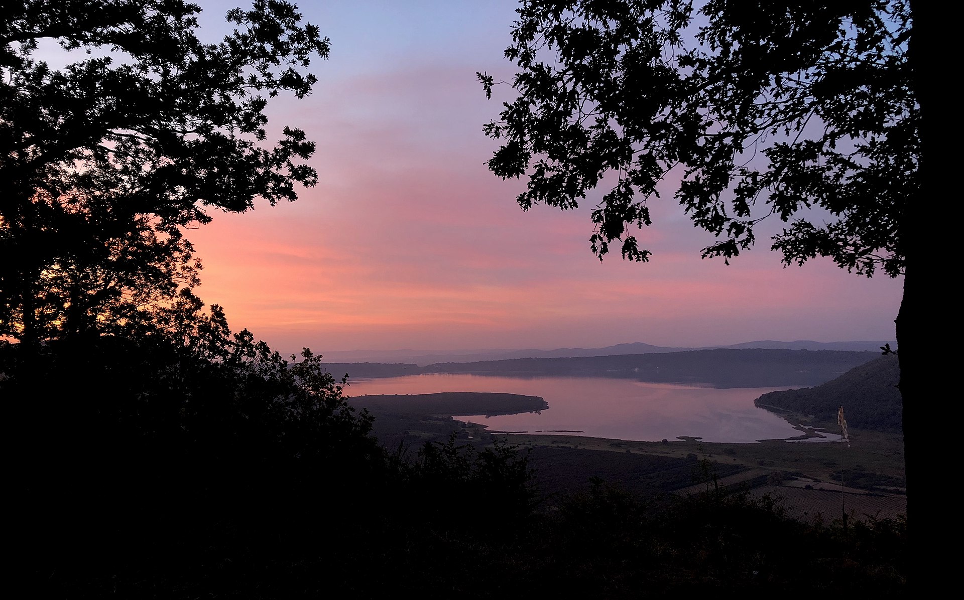 Il lago di Vico all’alba visto dal bosco dei Monti Cimini, con il cielo rosa sopra la caldera
