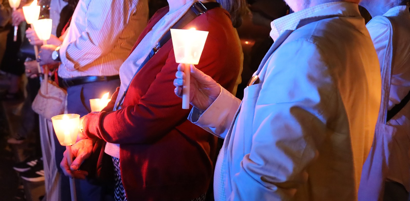 Mani di fedeli che reggono fiaccole accese in una processione serale