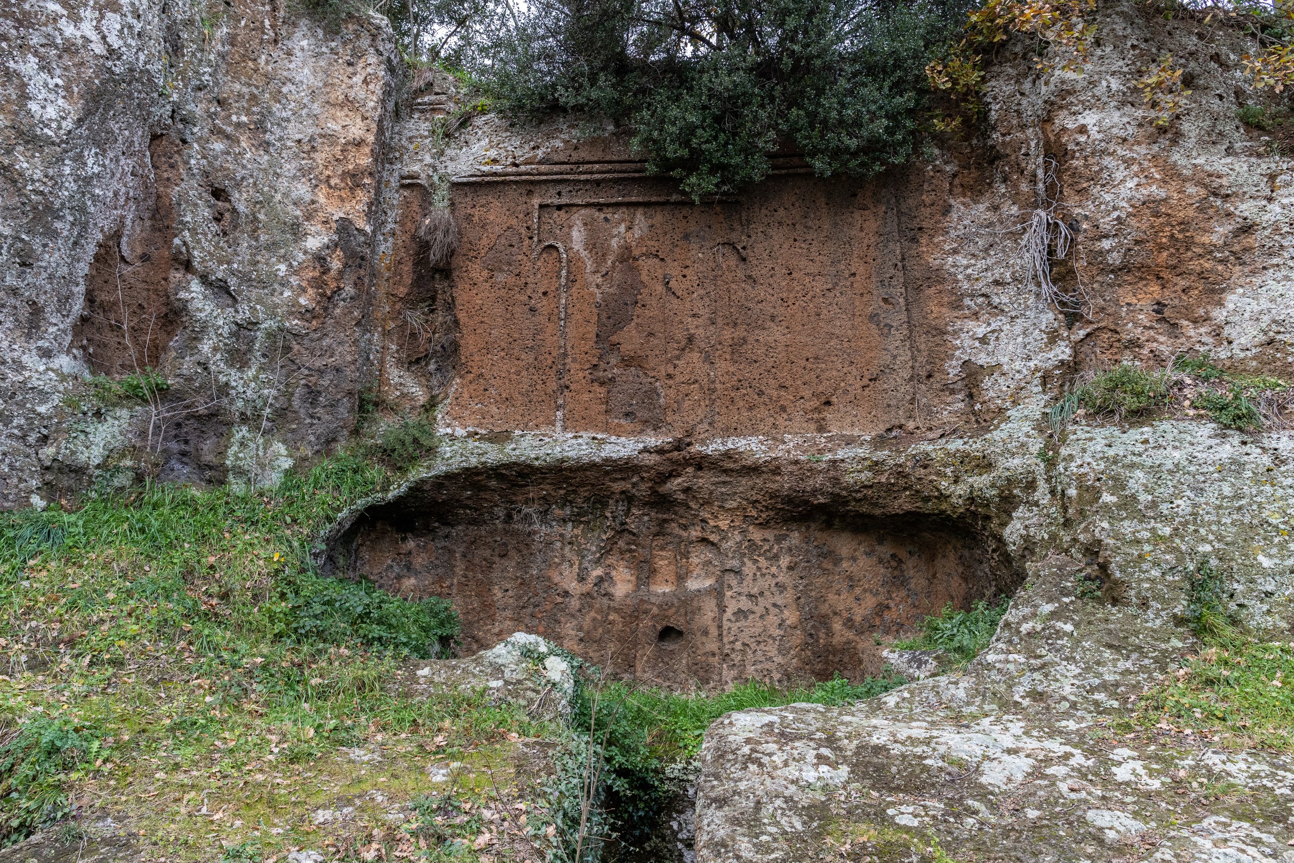 La facciata di una tomba etrusca scolpita nella parete di tufo della necropoli di Castel d’Asso, tra erba e lecci