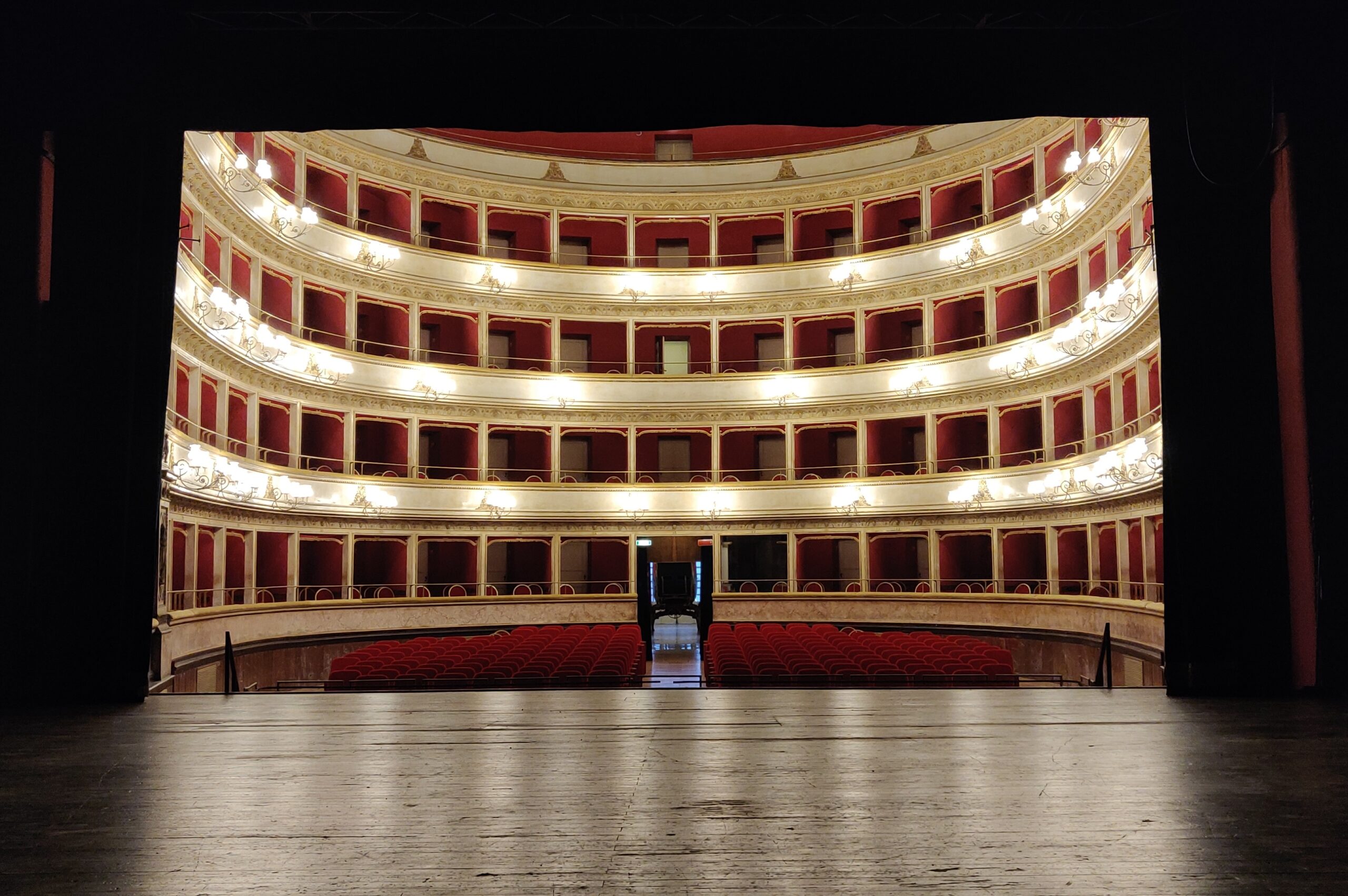 La sala del Teatro dell’Unione di Viterbo vista dal palco, con le poltrone rosse e quattro ordini di palchetti illuminati