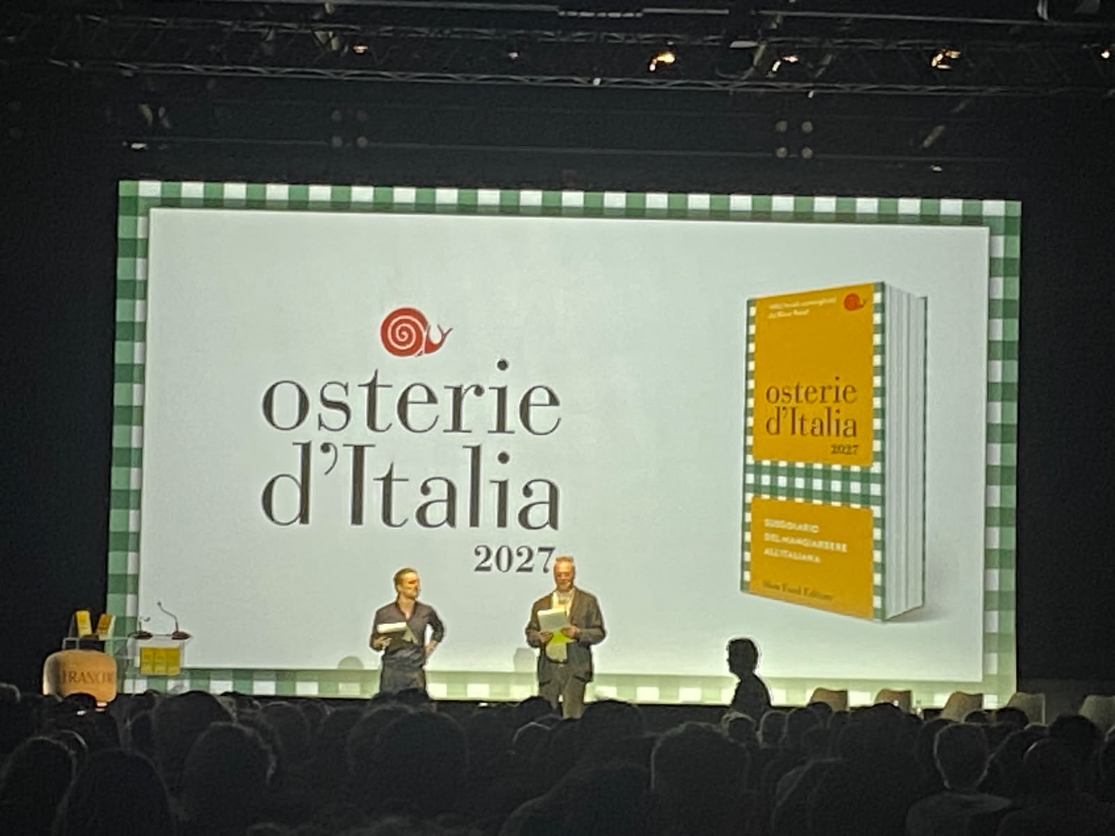 Il palco della presentazione di Osterie d’Italia 2027 alle OGR di Torino, con la copertina della guida proiettata sullo schermo