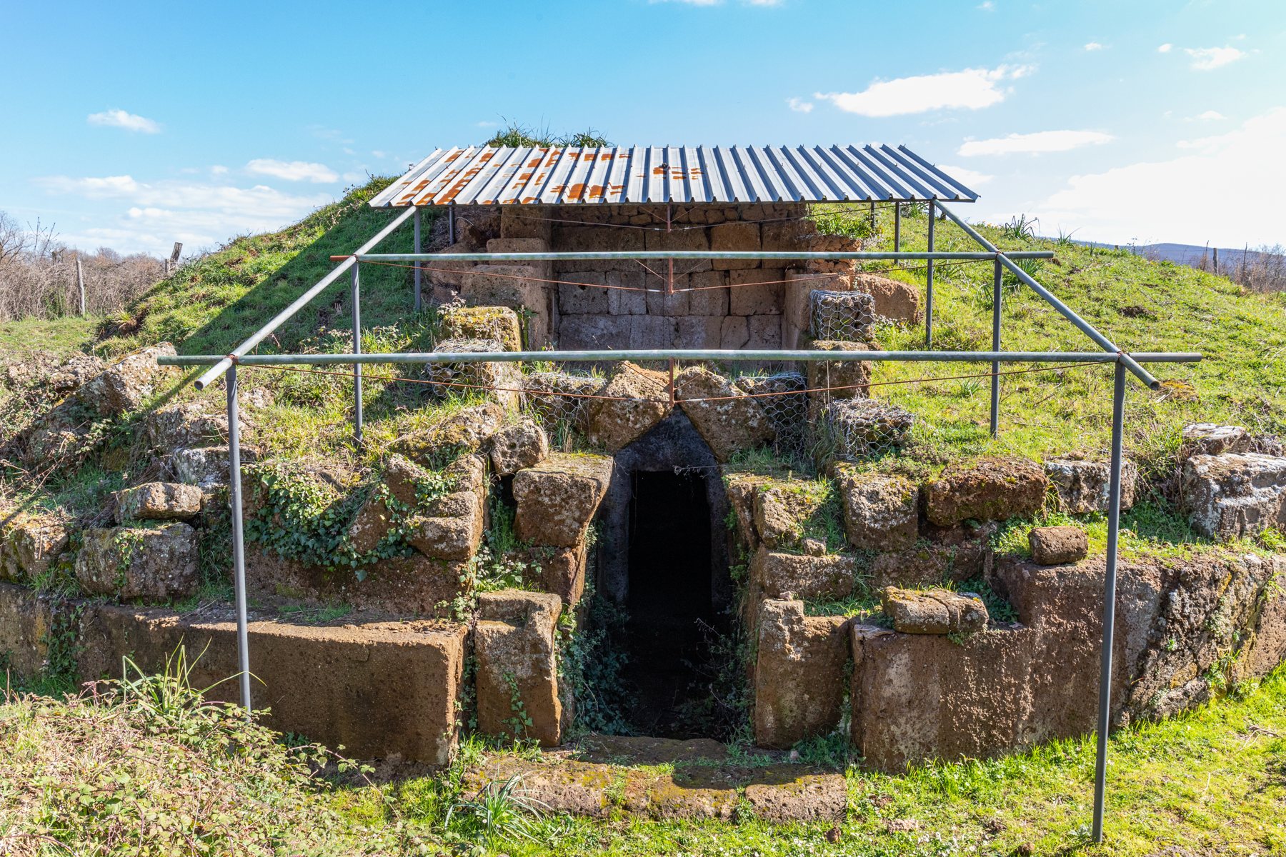 Tomba a tumulo etrusca con una tettoia di lamiera arrugginita su pali di metallo nella necropoli di San Giovenale